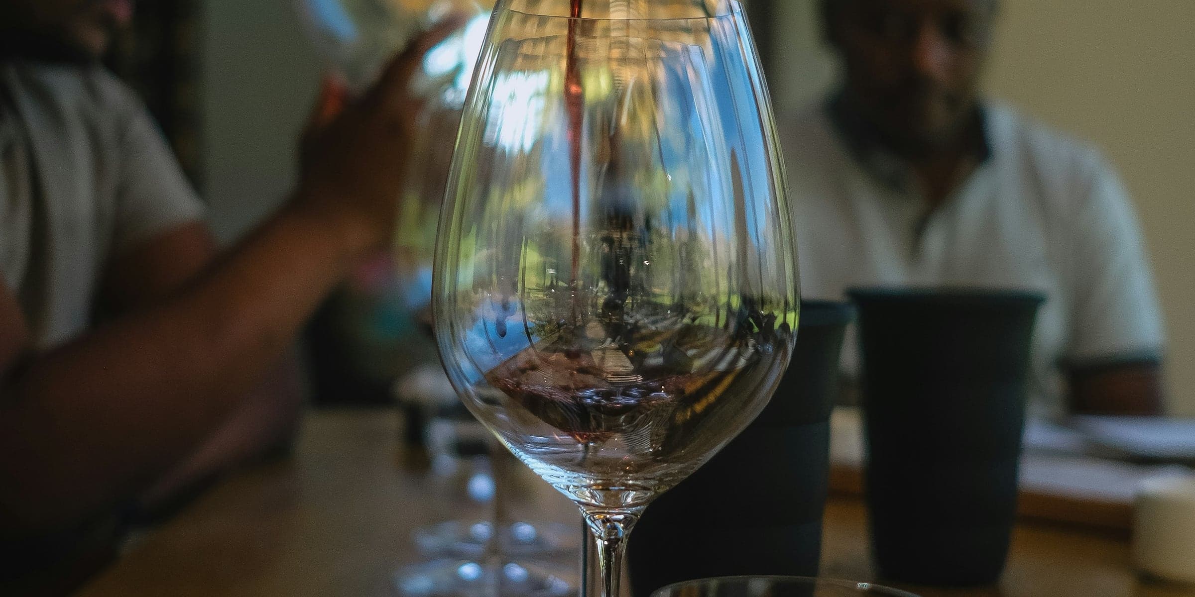 A bottle poured into a tasting glass while two people watch.